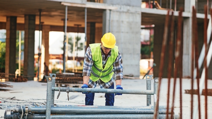 © iStock | Drazen Ein Bauarbeiter hebt Gerüstteile an.